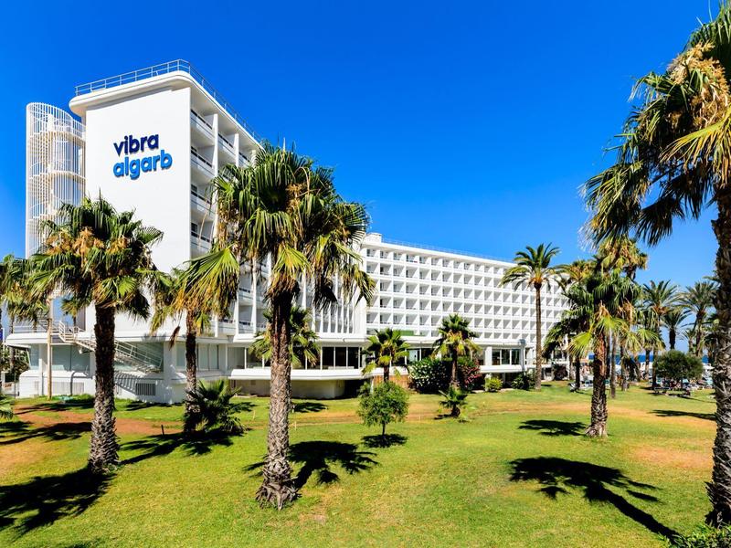 Modernes Hotelgebäude mit Palmen und grünem Rasen an einem sonnigen Tag