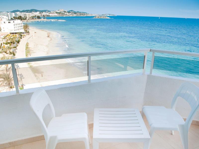 Balkon mit weißem Tisch und Stühlen mit Blick auf einen Sandstrand und das blaue Meer.