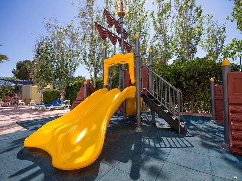 Żółta podwójna zjeżdżalnia na placu zabaw z drzewami i jasnoniebieskim niebem.