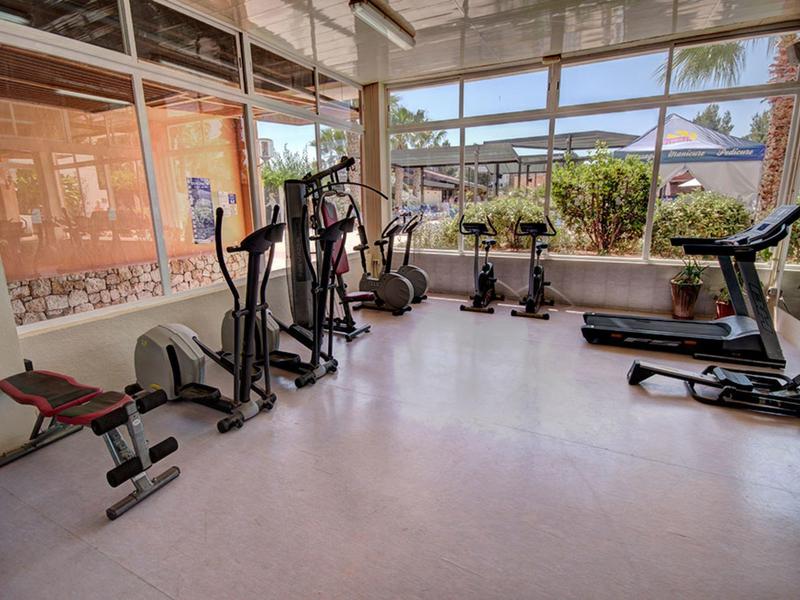 Siłownia z urządzeniami cardio i ciężarkami przed dużymi oknami z widokiem na zewnątrz.