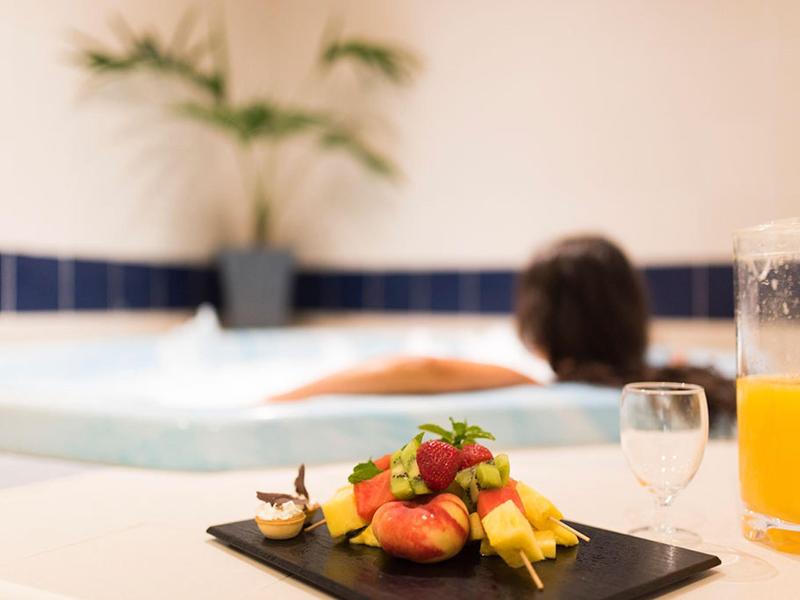 Zbliżenie świeżych owoców na talerzu z jacuzzi i osobą w tle.