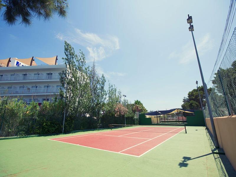 Kort tenisowy na świeżym powietrzu obok wielopiętrowego budynku hotelowego pod niebieskim niebem.