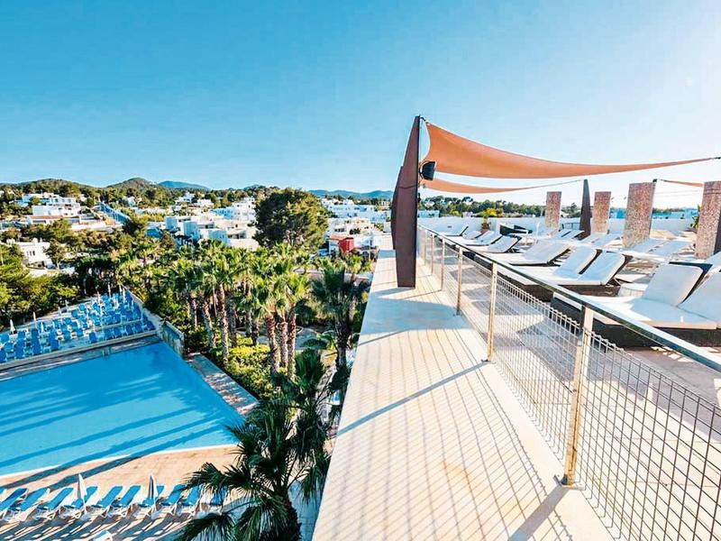 Widok z tarasu z leżakami i markizą na basen i otaczającą zieleń.