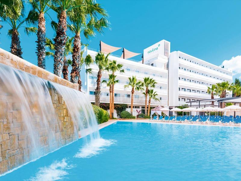 Nowoczesny hotel z dużym basenem, wodospadem i palmami pod jasnym niebem.