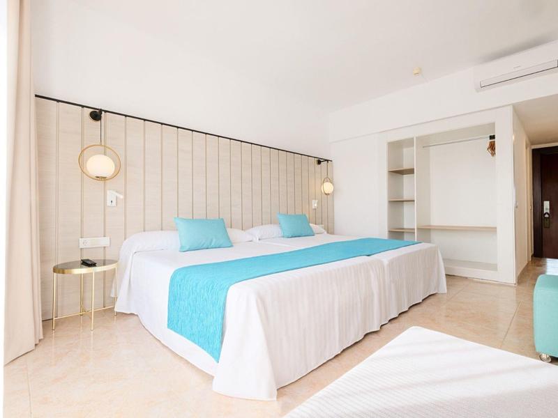 Jasny, nowoczesny pokój hotelowy z dużym łóżkiem podwójnym i niebieskimi poduszkami.