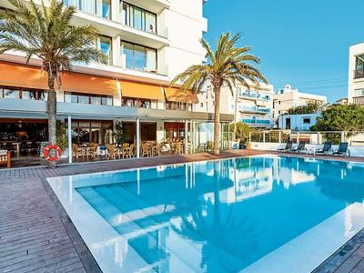 Moderní hotelový bazén se sluneční terasou a palmami pod jasně modrou oblohou.