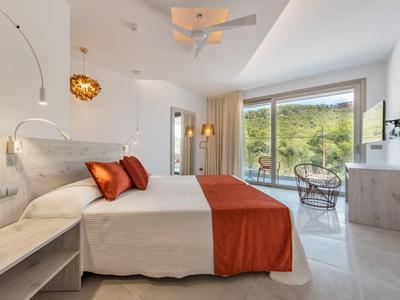 Moderní hotelový pokoj s manželskou postelí, oranžovým přehozem a přístupem na terasu s výhledem do přírody.