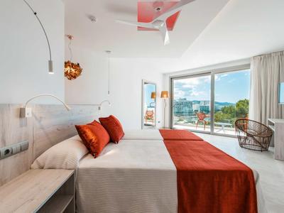 Moderní hotelový pokoj s velkou postelí, oranžovými akcenty a výhledem na terasu a moře.