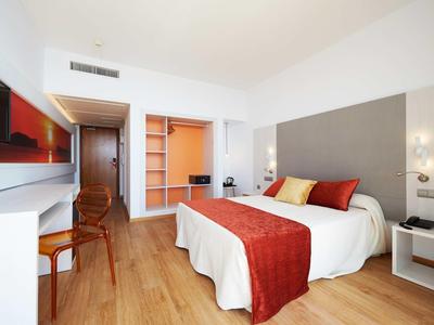 Moderní hotelový pokoj s dřevěnou podlahou a manželskou postelí s červenými akcenty.