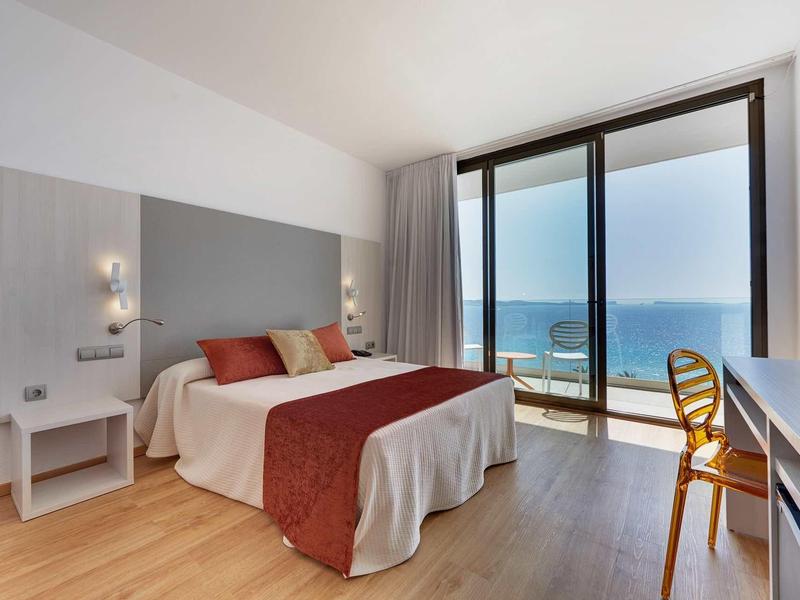 Moderní hotelový pokoj s manželskou postelí a výhledem na moře přes velká okna.