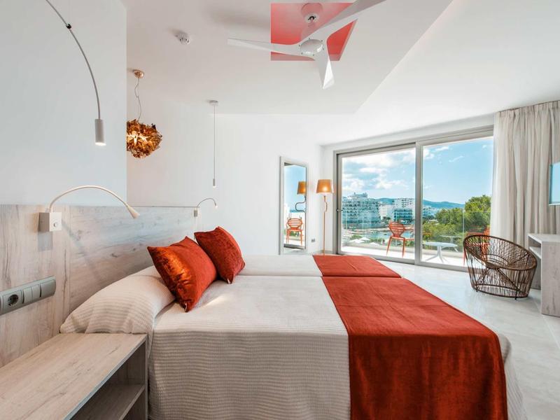 Moderní hotelový pokoj s velkou postelí, oranžovými akcenty a výhledem na terasu a moře.