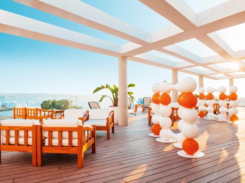 Otevřená hotelová terasa s posezením a oranžovo-bílými balonky za slunečného počasí.