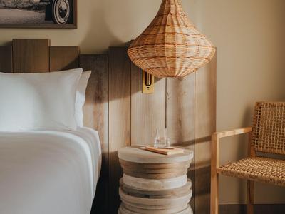 Gemütliches Hotelzimmer mit Holzbett, Nachttisch, Lampenschirm und Korbsessel.