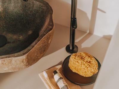 Moderner Wasserhahn neben einem steinernen Waschbecken auf einer weißen Oberfläche mit Seife und Tuch.