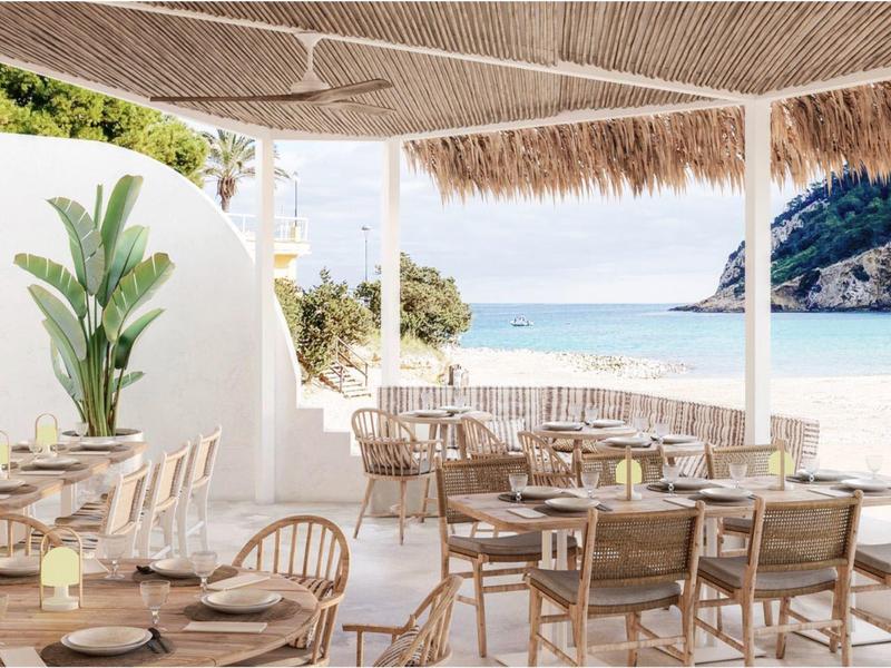 Espace repas en plein air avec mobilier en bois et vue sur la mer sous un toit de chaume.