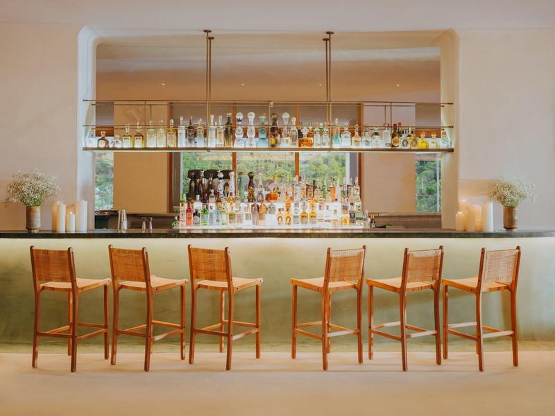 Espace bar d'hôtel moderne avec six chaises en bois et comptoir éclairé sous des étagères en verre.