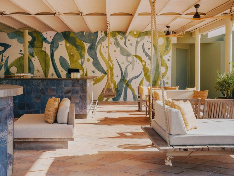 Espace extérieur lumineux avec des balançoires et une peinture murale colorée.