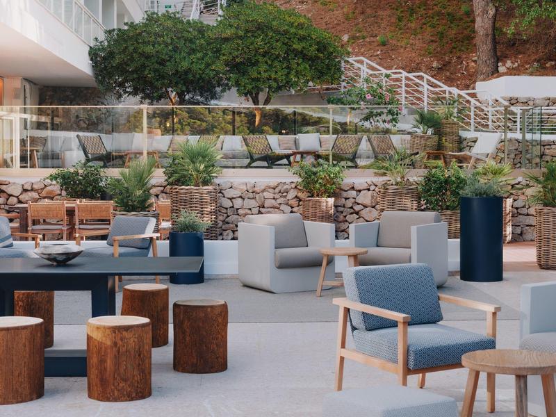 Espace extérieur moderne avec sièges en bois et rembourrés devant un mur de pierre planté.