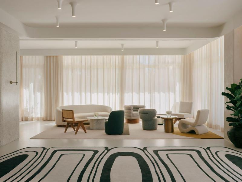 Chambre d'hôtel moderne avec grand lit, coin salon et grandes fenêtres avec rideaux.