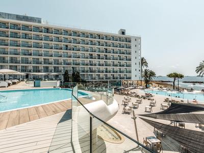 Moderní hotelový bazén s lehátky, skleněným zábradlím a výhledem na moře pod jasnou oblohou