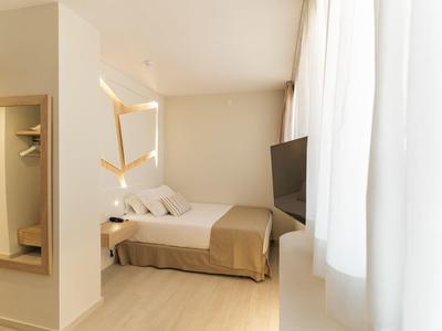 Světý hotelový pokoj s velkou postelí, televizí a závěsy u okna.