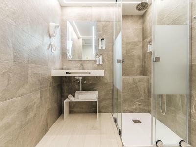 Moderní koupelna se sprchovým koutem, velkým zrcadlem a béžovými dlaždicemi.