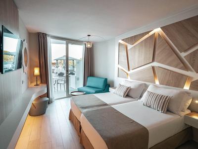 Moderní hotelový pokoj s manželskou postelí, pohovkou a balkonem s výhledem na moře.