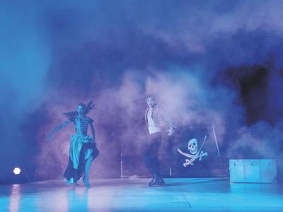 Due persone che ballano sul palco con nebbia blu e simbolo del pirata sullo sfondo.