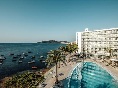 Hotel s velkým bazénem vedle pobřeží s loděmi a jasnou oblohou.