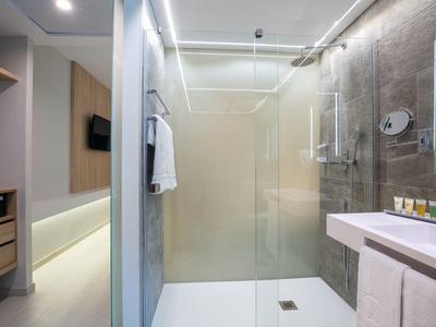 Moderní hotelová koupelna se skleněným sprchovým koutem, ručníky a umyvadlem se zrcadlem.