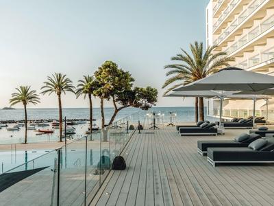 Hotelová terasa s lehátky, slunečníky a výhledem na moře a palmy při západu slunce.