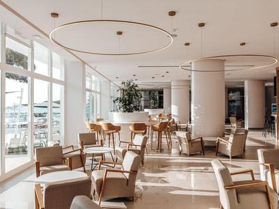 Světla hotelová restaurace s moderním nábytkem a velkým oknem s výhledem na vodu.