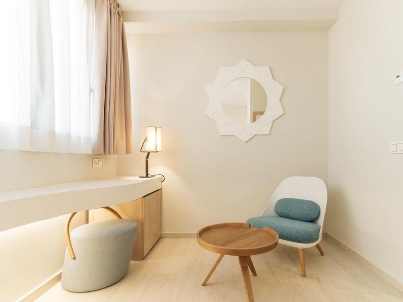 Světlá minimalistická místnost s modrým křeslem, kulatým dřevěným stolem a dekorativním zrcadlem.