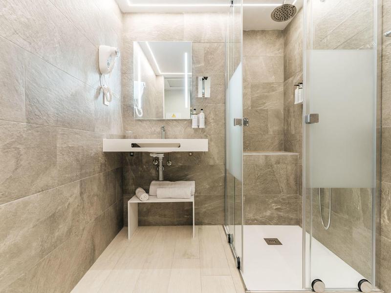Moderní koupelna se sprchovým koutem, velkým zrcadlem a béžovými dlaždicemi.