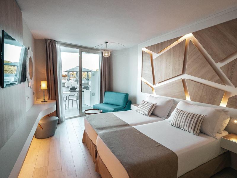 Moderní hotelový pokoj s manželskou postelí, pohovkou a balkonem s výhledem na moře.