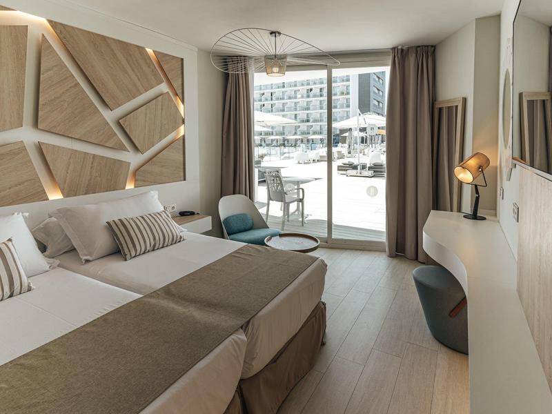 Moderní hotelový pokoj se dvěma postelemi, posezením a balkonem s výhledem na bazén.