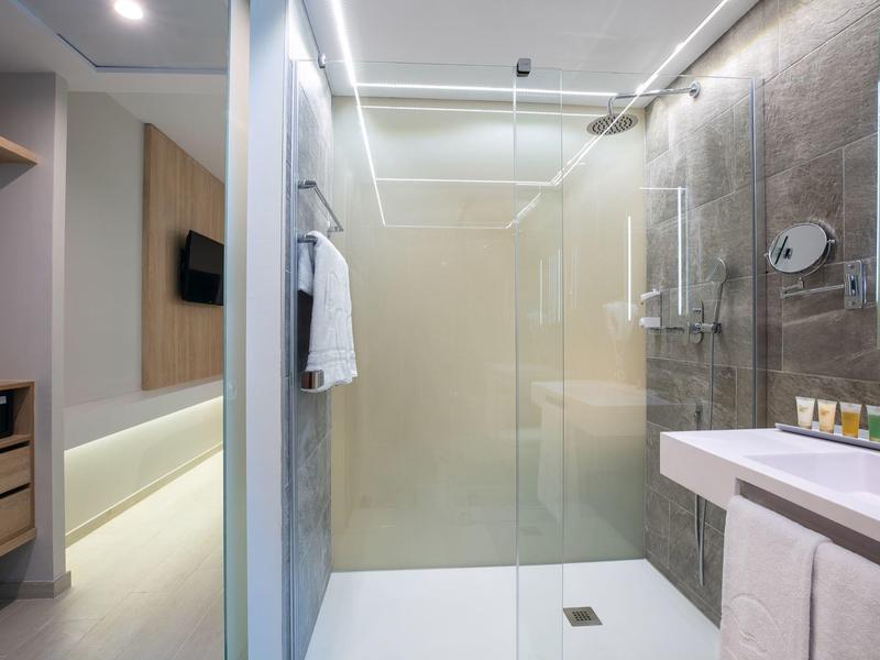 Moderní hotelová koupelna se skleněným sprchovým koutem, ručníky a umyvadlem se zrcadlem.