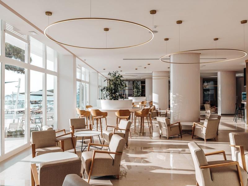 Světla hotelová restaurace s moderním nábytkem a velkým oknem s výhledem na vodu.