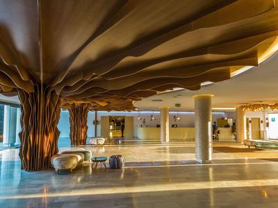 Großer offener Hotelbereich mit goldfarbenen, baumförmigen Säulen und Sitzgelegenheiten.