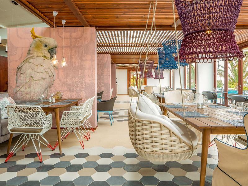Modern hotel dining area with woven chairs, wooden tables, and colorful hanging lamps.
