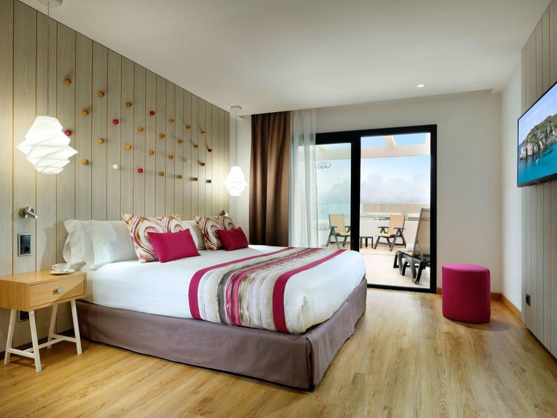 Modern hotel room with large bed, striped bedding, wooden floor, and balcony with sea view.