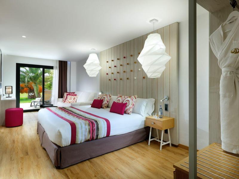 Modern hotel room with a double bed, wooden floor, and large window overlooking greenery.