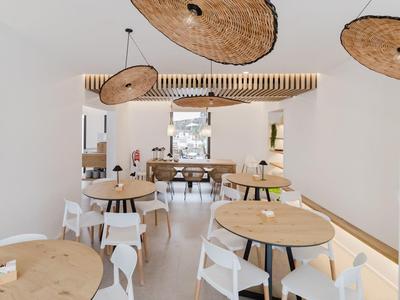 Moderne eetzaal met ronde houten tafels, witte stoelen en unieke plafondlampen.