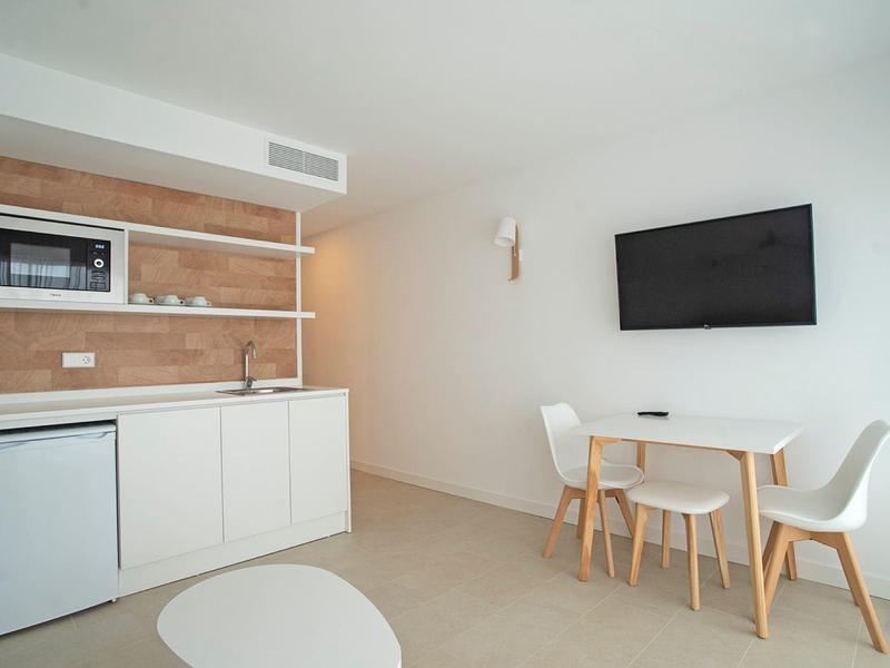 Moderne keuken met witte kasten, magnetron, koelkast en een kleine eettafel met twee stoelen.