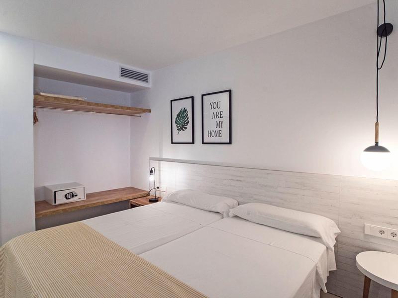 Modern hotelkamer met twee eenpersoonsbedden, minimalistische inrichting en open kledingopslag.