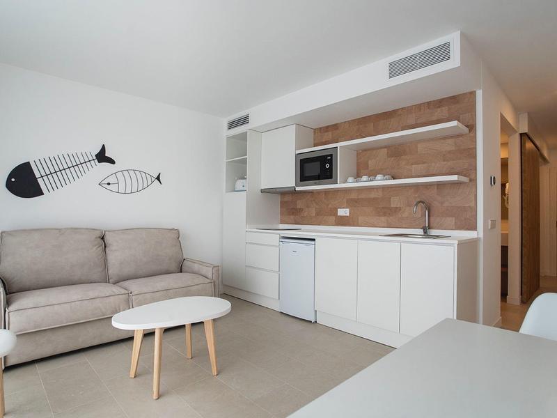 Kleine moderne hotelkeuken met slaapbank, koelkast en decoratieve viswanddecoratie.