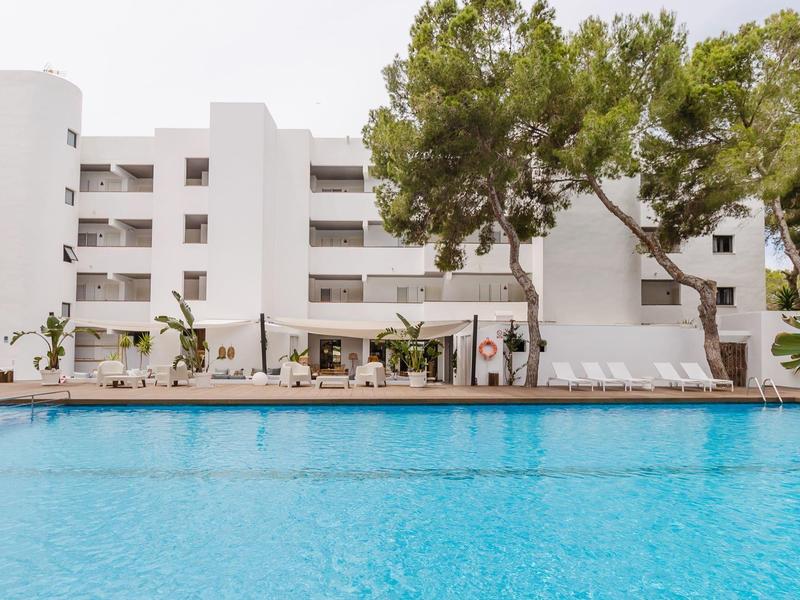 Hotel met meerlagig gebouw en groot buitenzwembad, omgeven door bomen en ligstoelen.