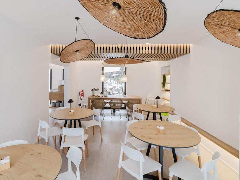 Moderne eetzaal met ronde houten tafels, witte stoelen en unieke plafondlampen.