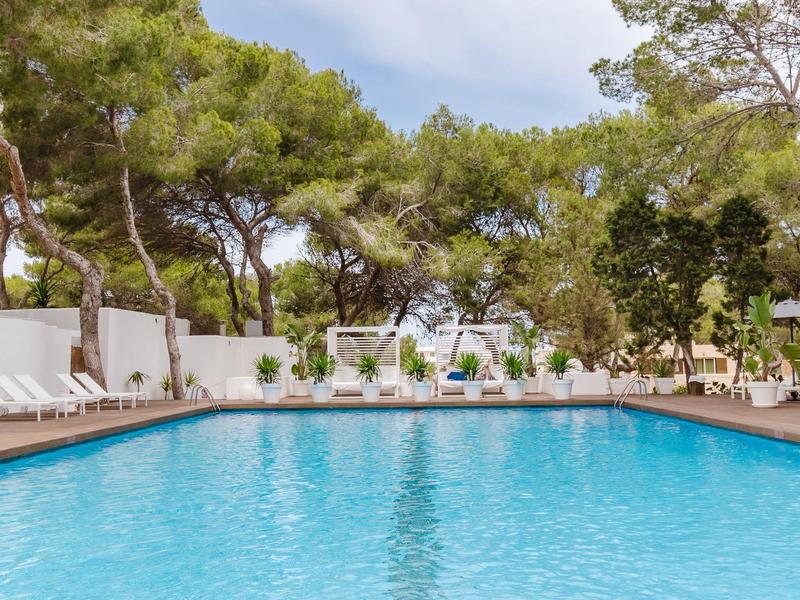 Groot zwembad met ligstoelen en bomen rondom een hotel tuin