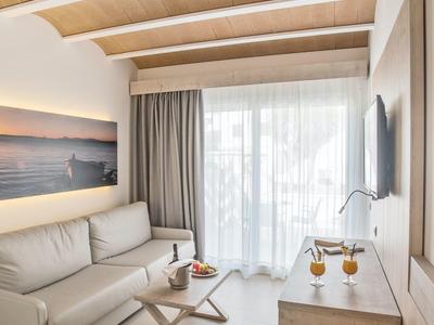 Moderní světlý obývací pokoj s dřevěnými trámy na stropě, šedou pohovkou a velkými okny se závěsy.